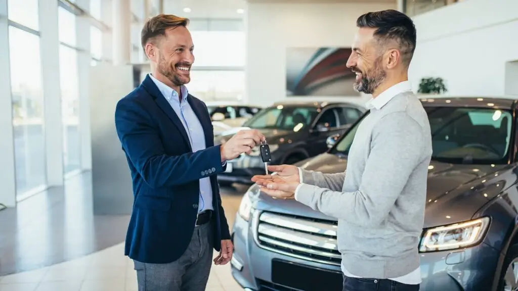 Salesperson handing car keys to a happy customer at a dealership