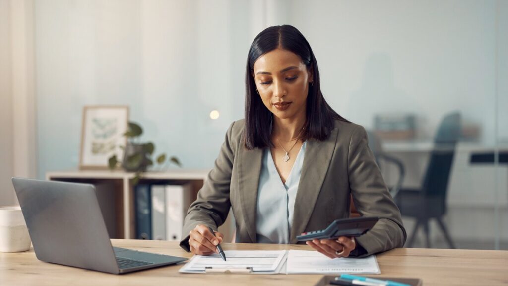 Professional at a desk reviewing insurance claims paperwork with laptop and calculator