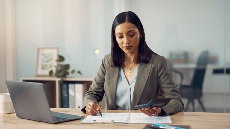 Professional at a desk reviewing insurance claims paperwork with laptop and calculator